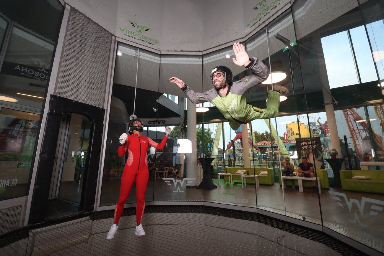 Zwei Personen in einem Windkanal, eine steht, eine fliegt.