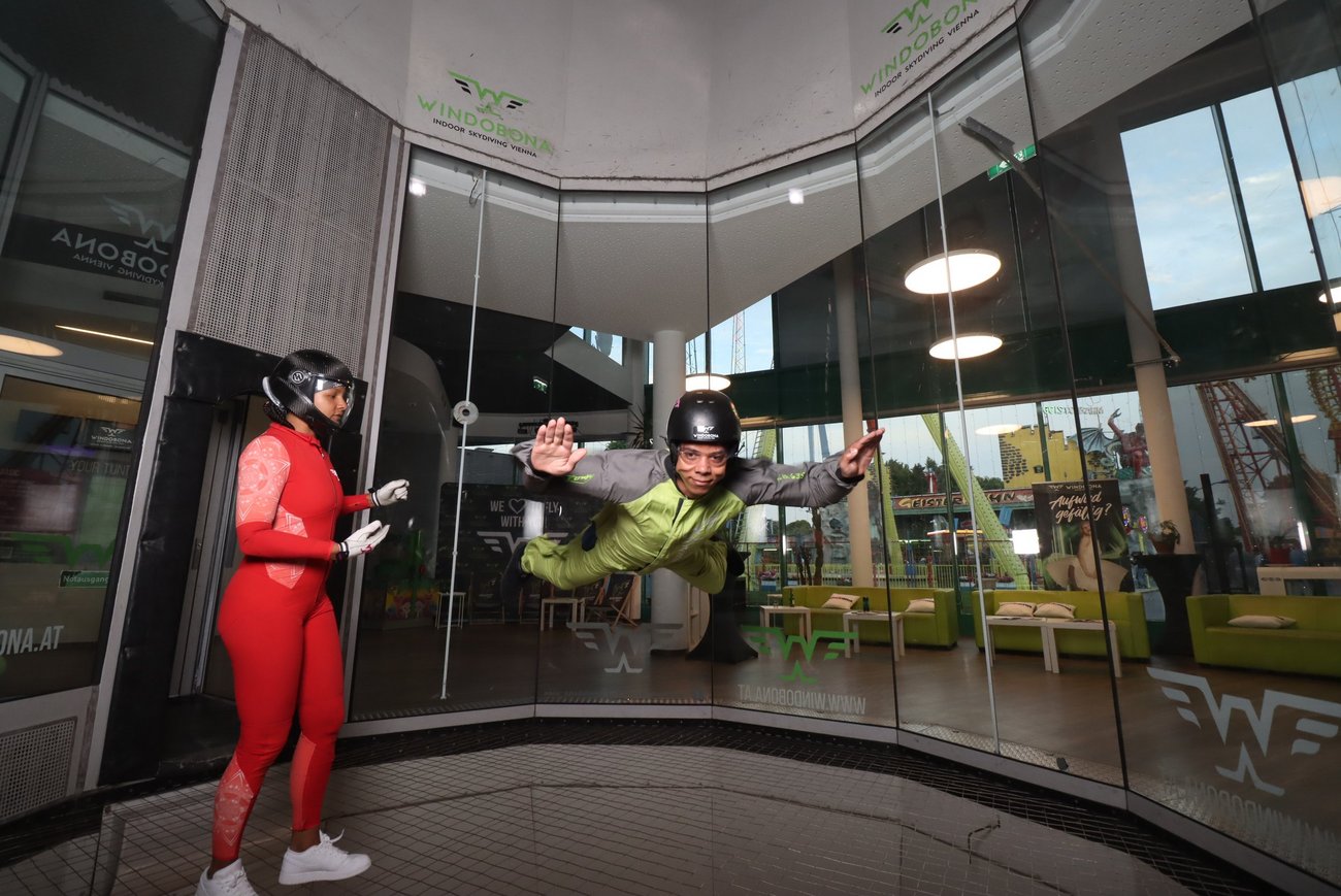 Zwei Personen in einem Windkanal, eine steht, eine fliegt.